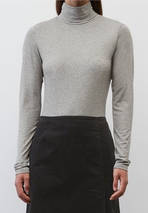 Un turtleneck gris à manches longues en tissu doux, au design ajusté, avec une texture lisse et un col roulé. Associé à une jupe noire.
