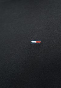 Μικρό ορθογώνιο έμβλημα με οριζόντιες ρίγες σε λευκό, μπλε και κόκκινο, κεντημένο σε μαύρο υφασμάτινο φόντο.