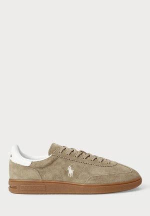 Beige suede sneakers with white accents and a logo. Features round toe, lace-up design, and a textured rubber sole.
