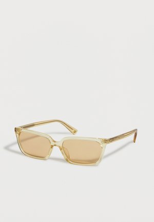 Lunettes de soleil rectangulaires transparentes jaune clair avec des verres teintés assortis posées sur un fond clair.