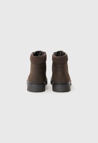 Botas de tobillo marrones con un exterior de ante texturizado, un cuello acolchonado y una suela negra de goma resistente. Detalle de costura visible.