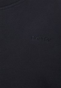 Zbliżenie czarnej prążkowanej tkaniny z subtelnym czarnym haftowanym logo Levi's na klatce piersiowej odzieży.