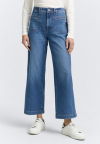 Jeans in denim azzurro chiaro a gamba larga con vita alta, dotati di tasche anteriori e posteriori e dettagli cuciti sull'orlo, abbinati a sneakers bianche.