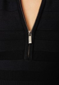 Černý pletený top s horizontálními pruhy, designem ve tvaru V a stříbrným zipem s texturovaným povrchem.