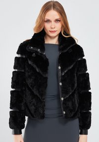 Black faux fur jacket with a glossy black leather collar and button closure. Features a textured, puffy design and ribbed cuffs.
