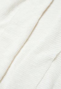 Valkoinen neulottu kangas, jossa on teksturoitu kuvio ja hienovaraisia vaakasuoria viivoja. Materiaali näyttää pehmeältä ja kevyeltä, mikä tekee siitä ihanteellisen kerrospukeutumiseen.