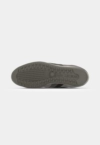 Suela de zapato gris con una superficie de goma texturizada que presenta patrones de agarre circulares y un diseño de rayas laterales. Logo de la marca embosado en el talón.