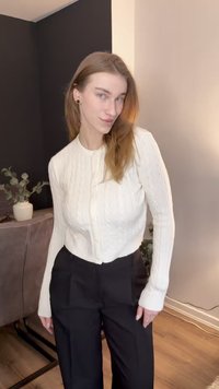 Witte kabelgebreide cardigan met een ronde halslijn en knoopsluiting. Gecombineerd met zwarte, hoog getailleerde broek. Eenvoudig, gestructureerd ontwerp.