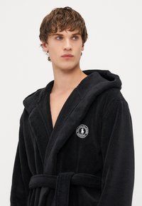 Svart bomulls terry morgenkåpe med hette, belte og logopatch. Har myk tekstur og design med sjalekrage.