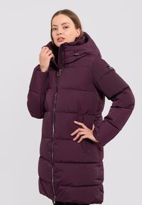 Lila Pufferjacke mit hohem Kragen, Reißverschluss und Seitentaschen. Verfügt über ein gestepptes Muster und eine Kapuze mit verstellbaren Kordeln.