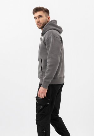 Grijze hoodie met een voorzak en een capuchon met trekkoord, gecombineerd met zwarte cargobroek met meerdere zakken en drukkers.