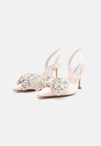 Bottines en satin beige à l'arrière ouvert, avec un bout pointu, ornées d'un nœud et d'accents en cristal, sur un talon fin.