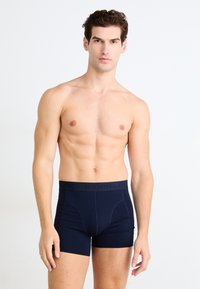 Námornícka modré boxerky vyrobené z mäkkej tkaniny majú diskrétny pás so vytlačeným brandingom, navrhnuté pre bezpečné nosenie a pohodlie.