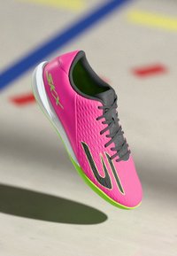 Sportovní boty s růžovým texturovaným svrškem, černými akcenty a zelenou podrážkou. Mají šněrování a lehký design vhodný pro atletické použití.