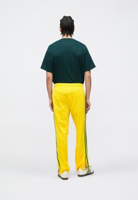 Zielona koszulka z krótkim rękawem o luźnym kroju, zestawiona z żółtymi spodniami sportowymi ozdobionymi zielono-niebieskimi bocznymi paskami i ze ściągaczem w pasie.