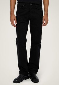 Jeans de mezclilla negros con corte recto, diseño de cinco bolsillos y costuras sutiles. Combinados con botas de cuero negras.