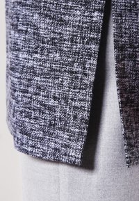 Grijs en zwart textuurstof die overlapt met een gladde lichtgrijze stof, en een close-up toont van gelaagde textielmaterialen.