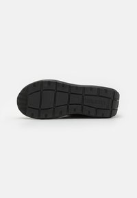 Svart gummisåle til sneakers med et teksturert mønster og segmentert dekk for bedre grep. Inkluderer logoavtrykk på siden.