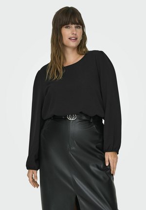 Blusa nera a maniche lunghe con scollo tondo e maniche arricciate, abbinata a una gonna in pelle nera a vita alta con uno spacco frontale.