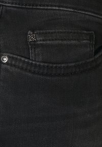 Svarta denimjeans med en liten framficka, en kontrasterande metallnabb och subtila sömmar längs kanterna. Slät textur.