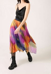 Plisserad kjol med livliga mönster i orange, rosa och lila akvarell; kombinerad med en svart satinöverdel och svarta snörade kängor.