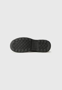 Black rubber shoe sole with a textured, patterned design. Features deep grooves for traction and a smooth heel section.
