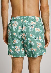 Zelene cvetne kopalke s elastičnim pasom, oranžno in belo hibiskusovo cvetje ter zadnji žep z črnimi poudarki.