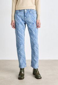Jeans de denim texturizado em azul claro, com corte reto. Apresenta cinco bolsos, uma fecho de botão e zip, usados com sapatos de salto verdes.