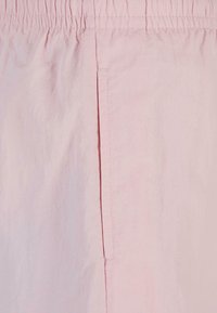 Lys rosa shorts laget av myk, lett stoff. Har elastisk midje og en sidelomme med en ren kantfinish.