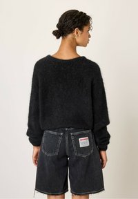 Juodas moheros megztinis su nuleistais pečiais, derinamas su išblukusiais juodais džinsiniais šortais, turinčiais ženklinimą ant galinio kišenės.