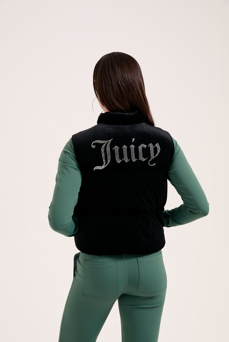 Črn brezrokavnik z visokim ovratnikom, ki vsebuje kristale, ki oblikujejo besedo "Juicy" na hrbtu. Obdan z dolgimi zelenimi rokavi in usklajenimi hlačami.