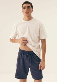 Biała bawełniana koszulka z krótkim rękawem w połączeniu z ciemnoniebieskimi szortami z elastycznym paskiem w talii i detalem w postaci sznurków.