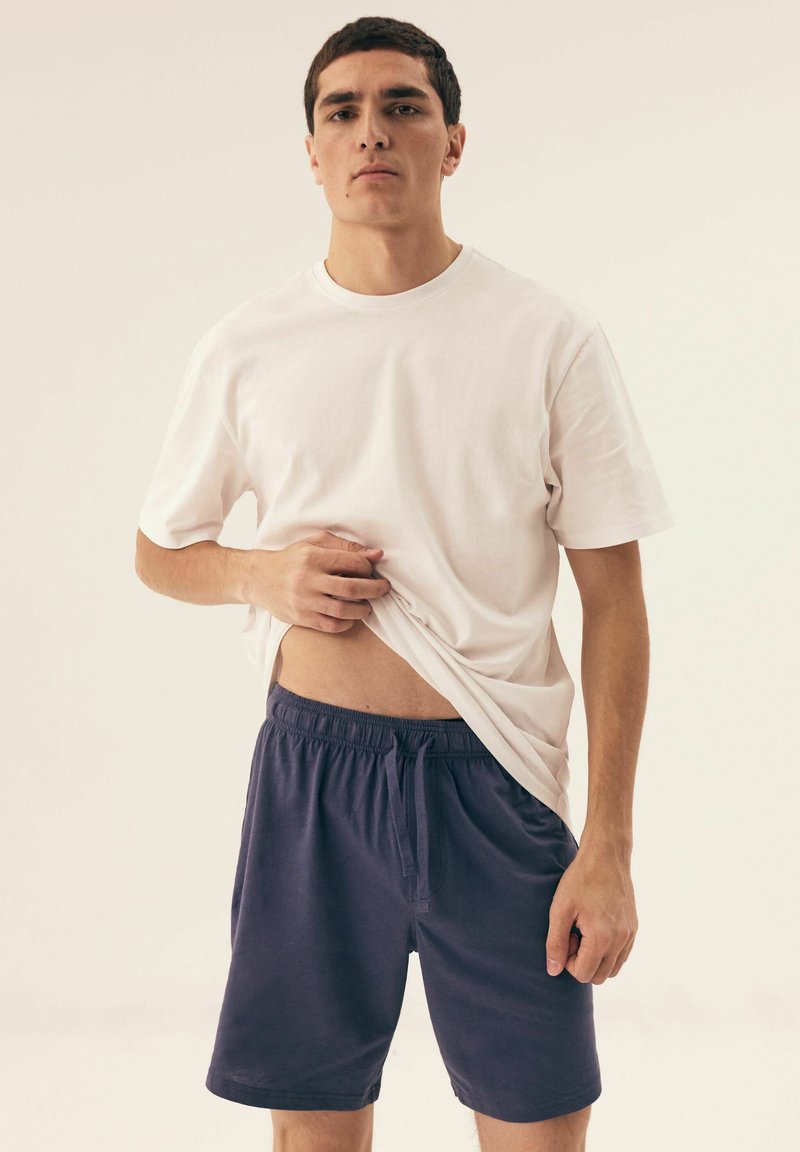 Biała bawełniana koszulka z krótkim rękawem w połączeniu z ciemnoniebieskimi szortami z elastycznym paskiem w talii i detalem w postaci sznurków.