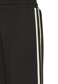 Pantaloni della tuta neri con vita regolabile, caratterizzati da due strisce verticali bianche sui lati. Texture morbida e taglio dritto.