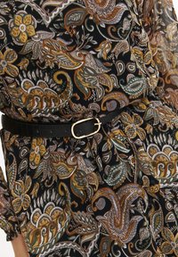 Schwarzer Stoff mit aufwendigen Paisley- und Blumendesigns in Gold, Grün und Weiß, tailliert mit einem schwarzen Gürtel.