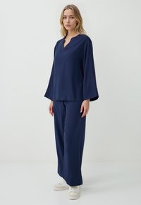 Navyblauw twee-delig outfit met een losse top met lange mouwen en een V-hals, en rechte broek. Gladde textuur, minimale details en casual pasvorm.