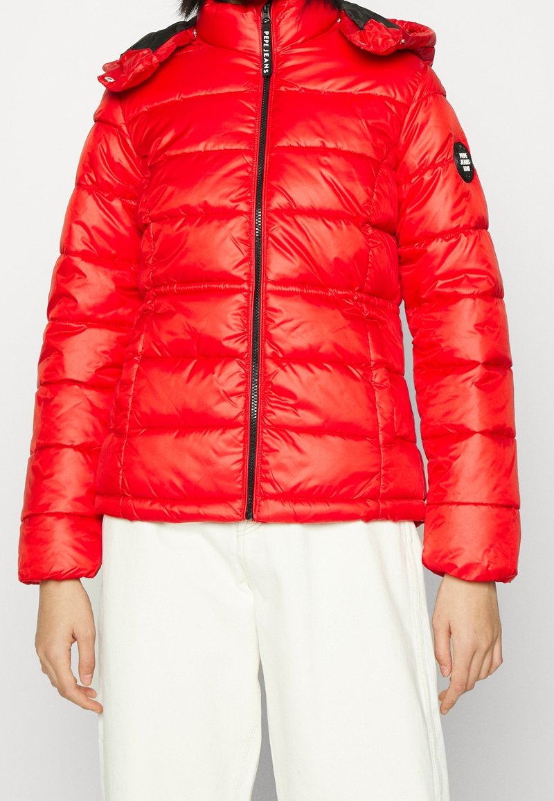 Röd puffjacka med dragkedja framtill, svarta detaljer på kragen och ett quiltat mönster. Har en tajt passform och en uppstående krage.