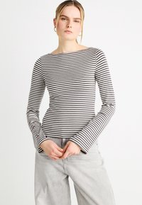 Μπλούζα με μακριά μανίκια σε γκρι και λευκές οριζόντιες ρίγες, με λαιμόκοψη τύπου βάρκα και φαρδιά μανσέτα, συνδυασμένη με ανοιχτό γκρι τζιν.