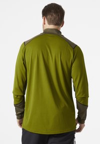 Zelená košile s dlouhým rukávem a kontrastními tmavě zelenými akcenty, strukturovaná tkanina a ploché švy, s vysokým límcem a prodlouženými rukávy.