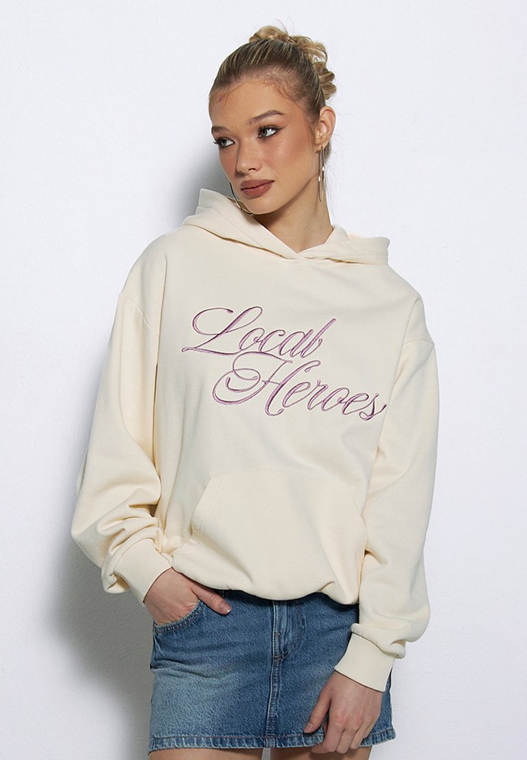 Kremowa bluza z kapturem, z przednią kieszenią, z haftowanym napisem "Local Heroes" w różowym stylu. W zestawieniu z dżinsową spódnicą.