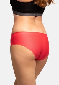 Culotte rouge pour femmes en matériau lisse et extensible. Présente une taille haute et un design sans coutures pour le confort.
