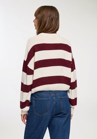 Sweter dzianinowy w burgundowe i kremowe poziome paski, z luźnym krojem, obniżonymi ramionami i wysokim kołnierzem; w zestawieniu z jeansami o wysokim stanie.