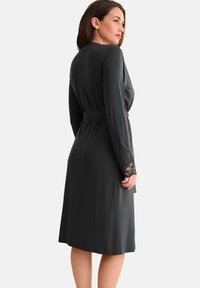 Robe enveloppante gris foncé avec des manches longues, taille ceinturée et accents en dentelle aux poignets, fabriquée dans un matériau lisse et léger.