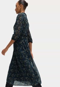 Długa, przezroczysta granatowa sukienka z kwiatowym wzorem w niebieskie i żółte kolory, z rękawami trzy czwarte, dopasowaną talią i zwiewną spódnicą.