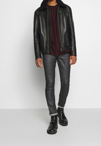 Svart läderjacka med pälskrage, kombinerad med en rödrandig skjorta, mörka jeans och svarta ankelstövlar. Snygg, åtsittande design.