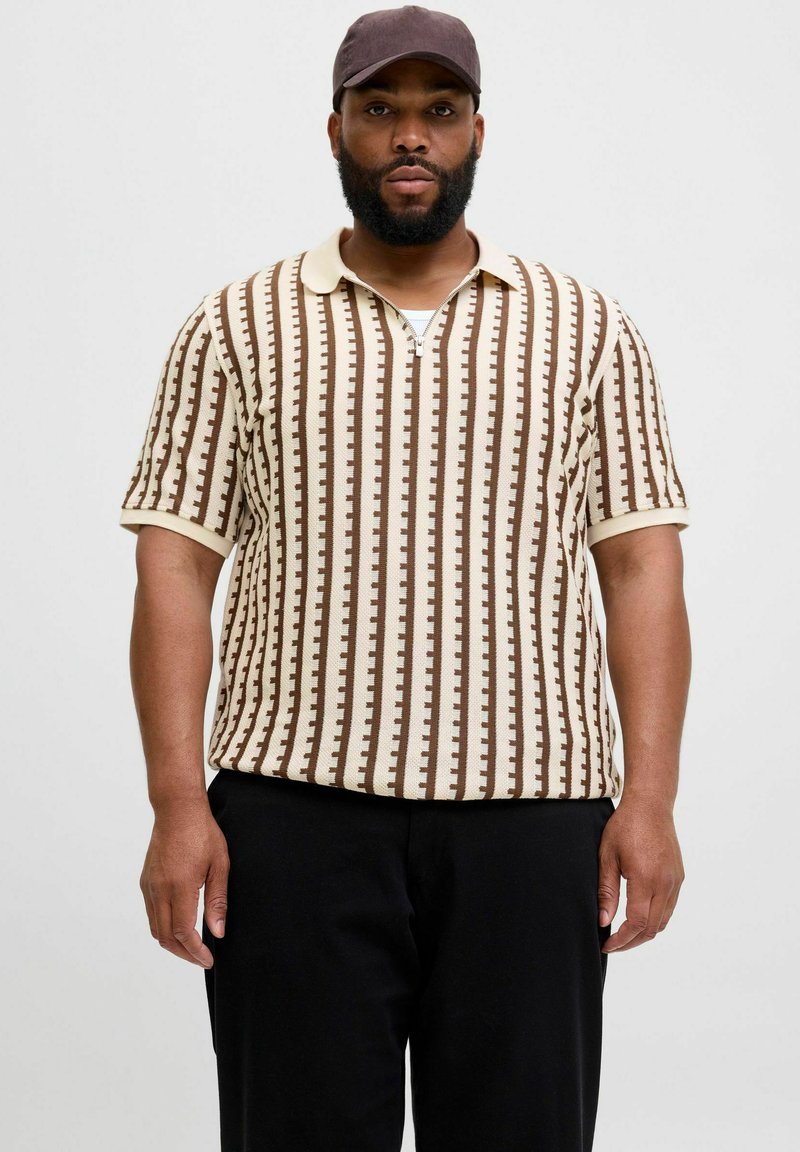 Polo a maniche corte con un motivo a righe marroni e crema, realizzato in tessuto texturizzato con colletto e chiusura a zip frontale, abbinato a pantaloni neri.