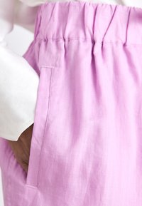 Shorts en lin rose avec une taille élastique et des poches latérales. Le tissu a une apparence douce et légèrement texturée.