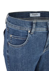 Granatowe dżinsy o prostym kroju, pięcioma kieszeniami, subtelnymi przeszyciami oraz metką na talii z logo marki. Powierzchnia wydaje się gładka.