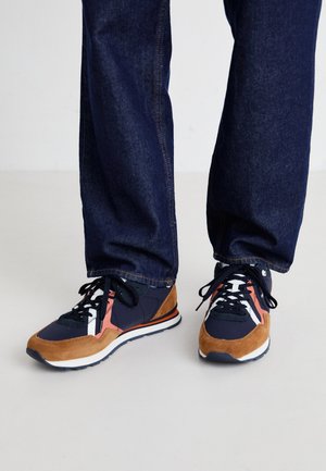 Zapatillas navy y marrón con materiales de ante y malla, que presentan acentos rosa y blanco, cordones negros y una suela de goma blanca.