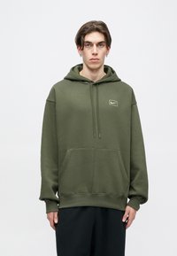 Ελιά πράσινη φούτερ με καγκουρό τσέπη, κουκούλα με κορδόνι και μικρό λογότυπο στο στήθος. Μαλακό ύφασμα με άνετη εφαρμογή.